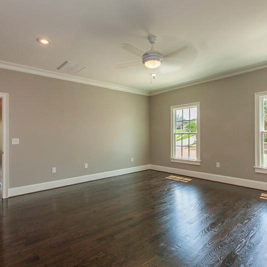 Empty room with light brown walls, dark wood floors, two windows letting in natural light, a ceiling fan with a light, and an open door leading to another room—an excellent example of the attention to detail provided by midlands contractors and custom home builders.