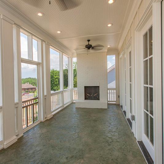Spacious screened-in porch with a ceiling fan, fireplace, and large windows, overlooking a neighborhood of new homes and greenery under a partly cloudy sky—an inviting feature in this thoughtfully designed new construction home.