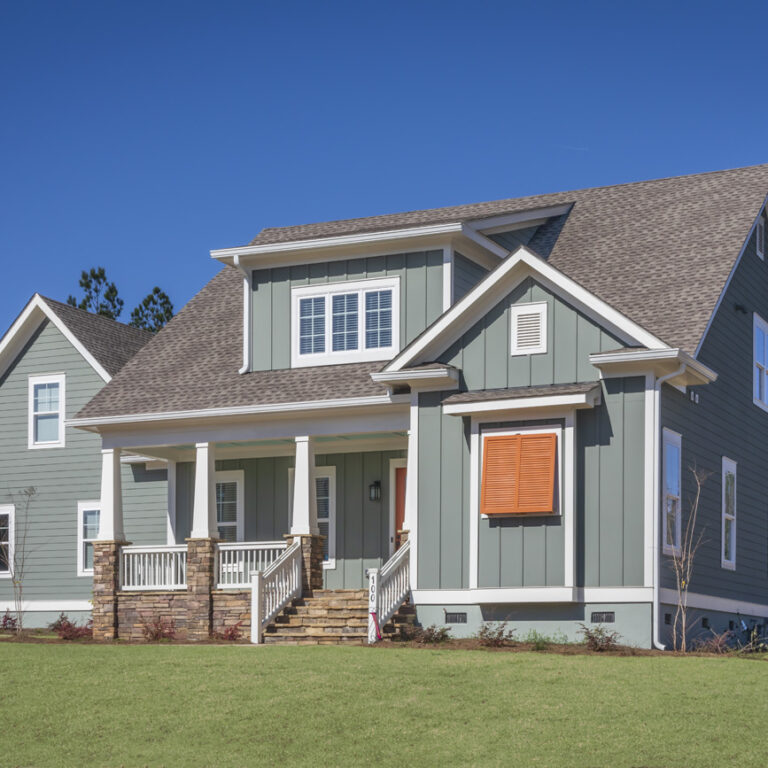 A modern two-story new construction home with green siding, white trim, a covered front porch, and wooden steps, set on a grassy lawn under a clear blue sky. Crafted by Midlands contractors, this residence features a custom floor plan designed for comfortable living.