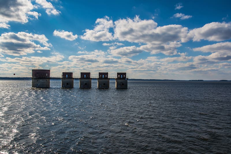 Lake-Murray-South-Carolina Five square concrete structures stand in a row over a large body of water under a partly cloudy sky, with sunlight reflecting on the rippling surface—a striking reminder of the innovation and strength that custom home builders bring to each new construction home.