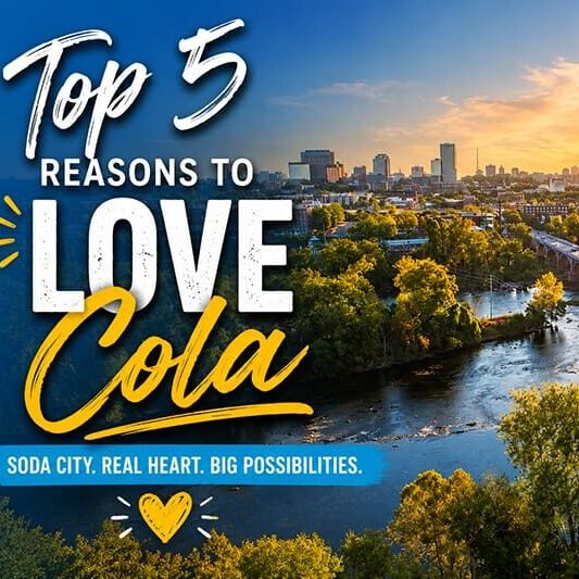 A city skyline at sunset with a river and trees in the foreground. Text reads: Top 5 Reasons to Love Cola. Soda City. Real Heart. Big Possibilities—including new homes designed with your lifestyle in mind. A yellow heart appears at the bottom.