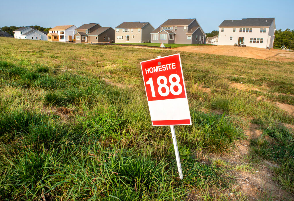 A sign marked HOMESITE 188 stands in a grassy home lot in front of several newly built houses, representing an available property selection.