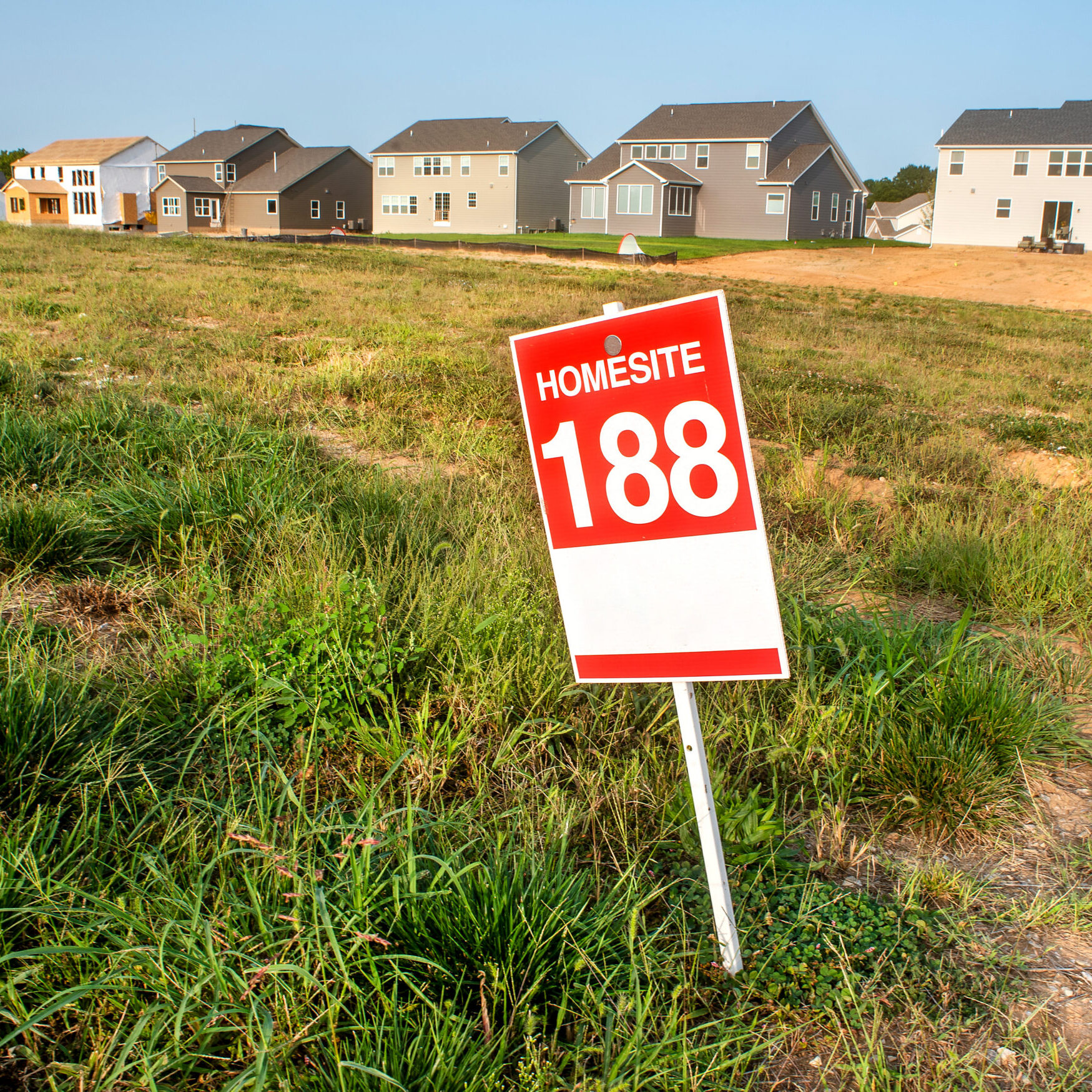 A sign marked HOMESITE 188 stands in a grassy home lot in front of several newly built houses, representing an available property selection.
